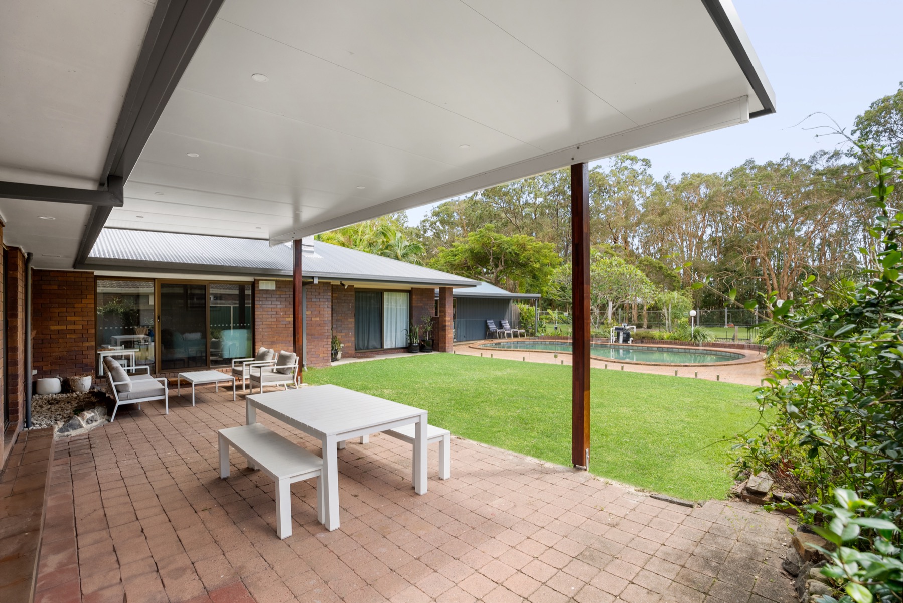 Insulated flyover patio over a paved outdoor dining area, looking out to pool and lawn